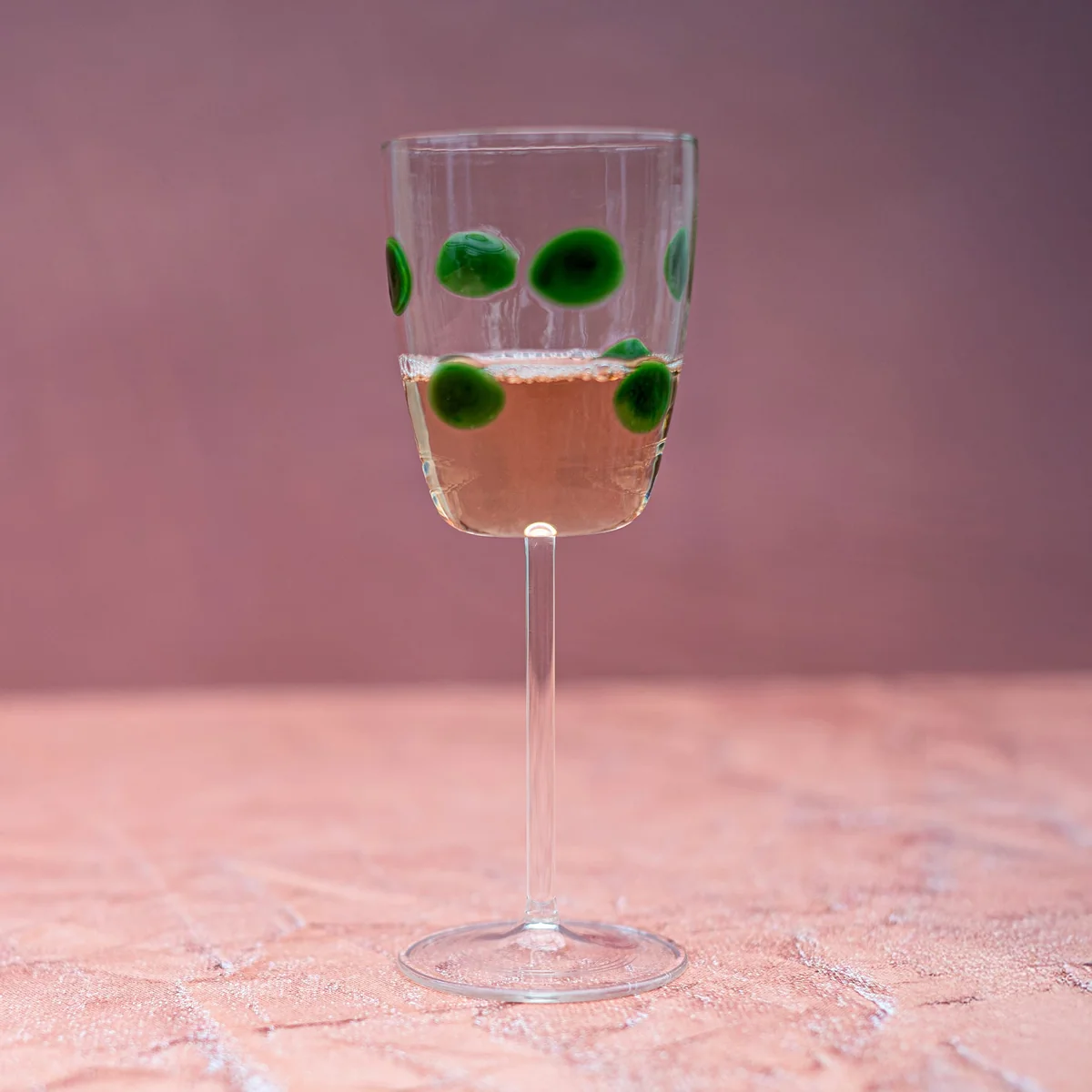 wine glass with green dots shown filled with wine in a neutral setting