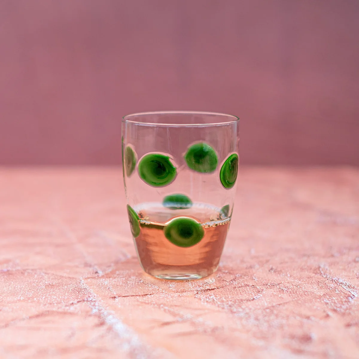 tumbler glass with green dots shown filled with a beverage in a neutral setting
