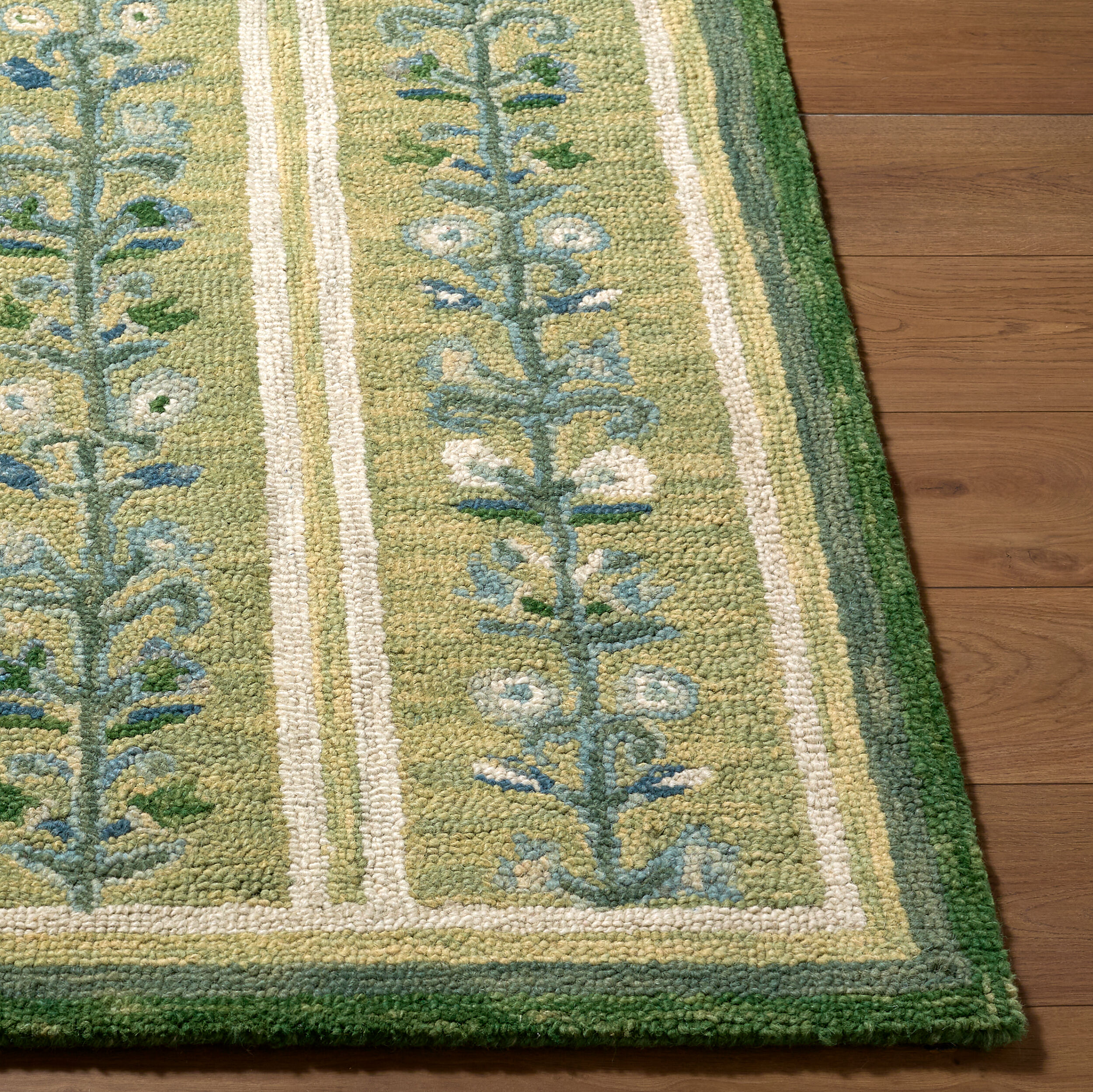 detail of hand tufted green rug with repeating blue and cream floral vine motifs, ivory stripes, and a dark green border