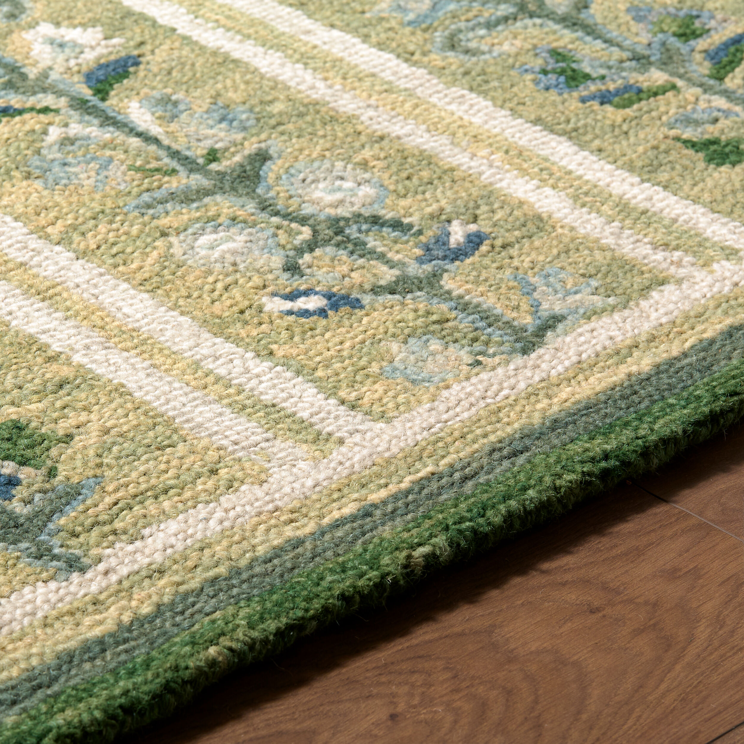 detail of hand tufted green rug with repeating blue and cream floral vine motifs, ivory stripes, and a dark green border