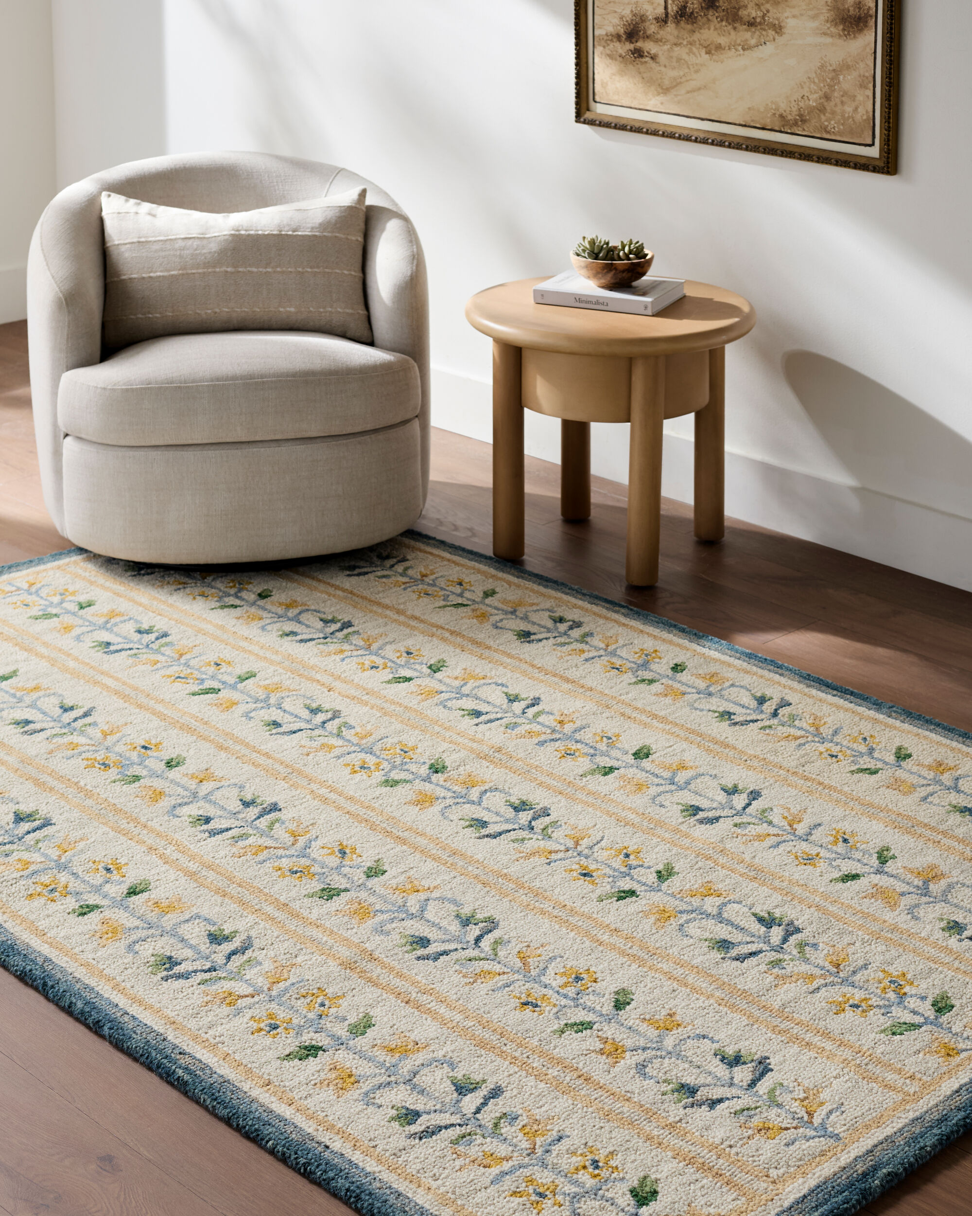 lifestyle image of a hand tufted ivory rug with repeating blue and gold floral vine motifs, gold stripes, and a dark blue border