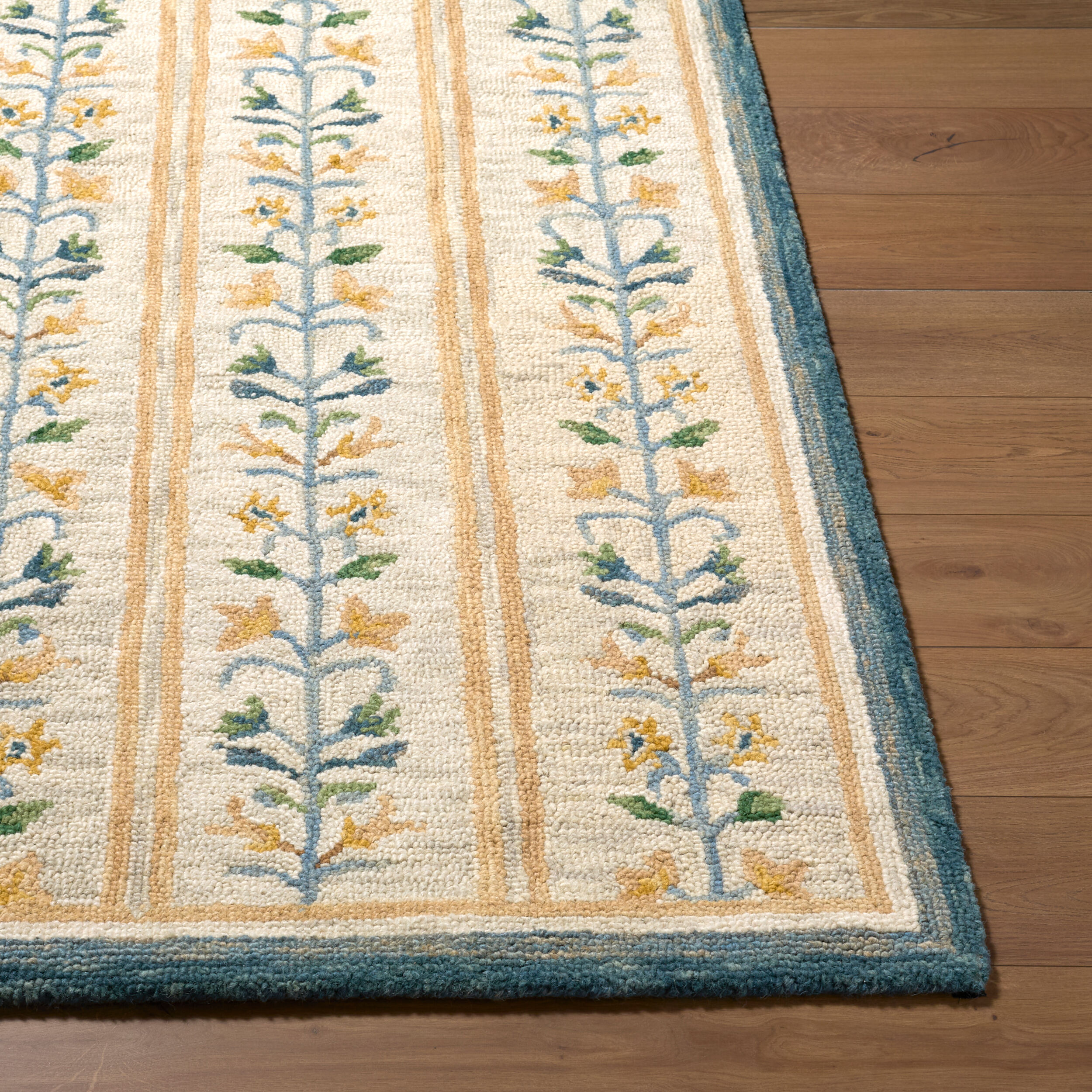detail of hand tufted ivory rug with repeating blue and gold floral vine motifs, gold stripes, and a dark blue border