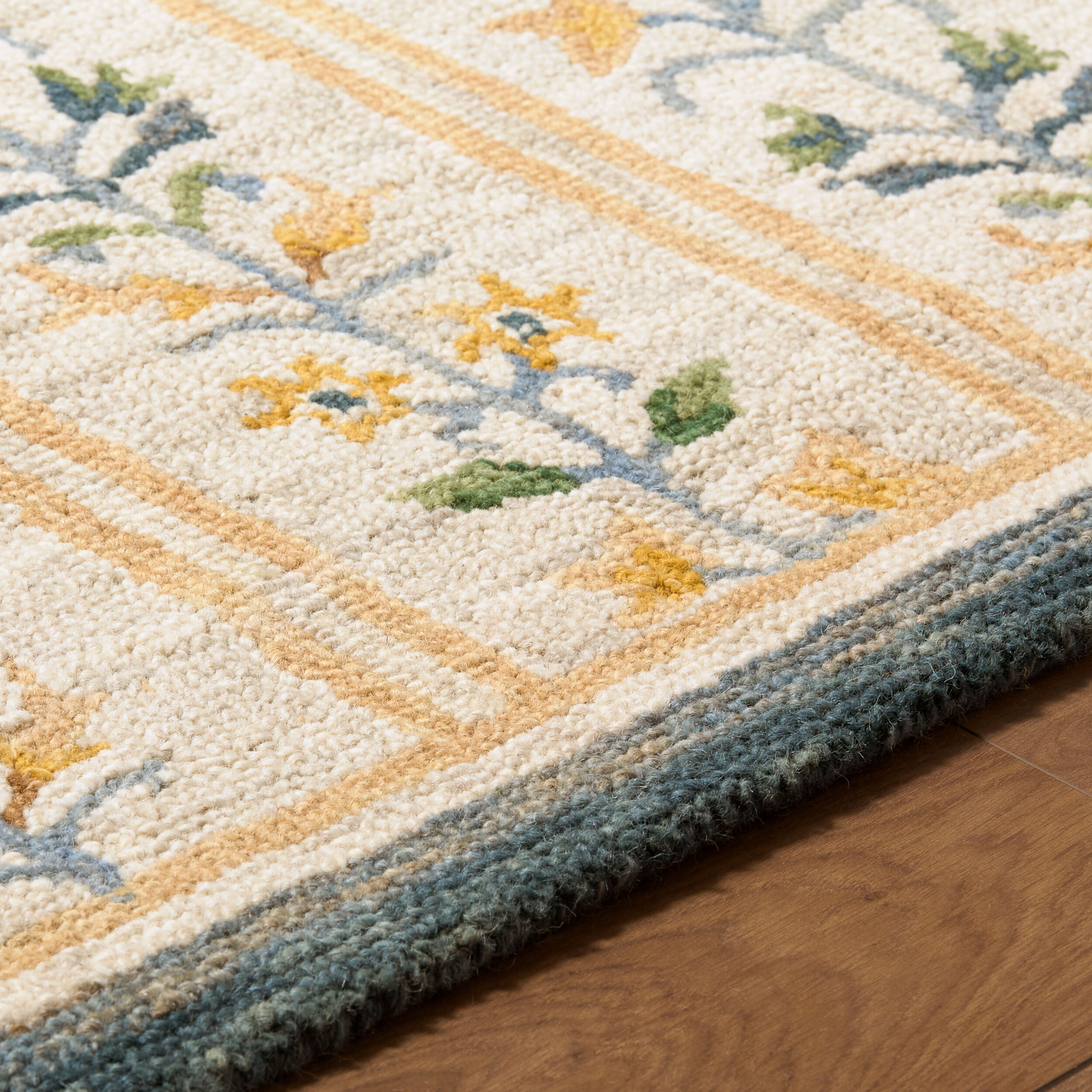 detail of hand tufted ivory rug with repeating blue and gold floral vine motifs, gold stripes, and a dark blue border