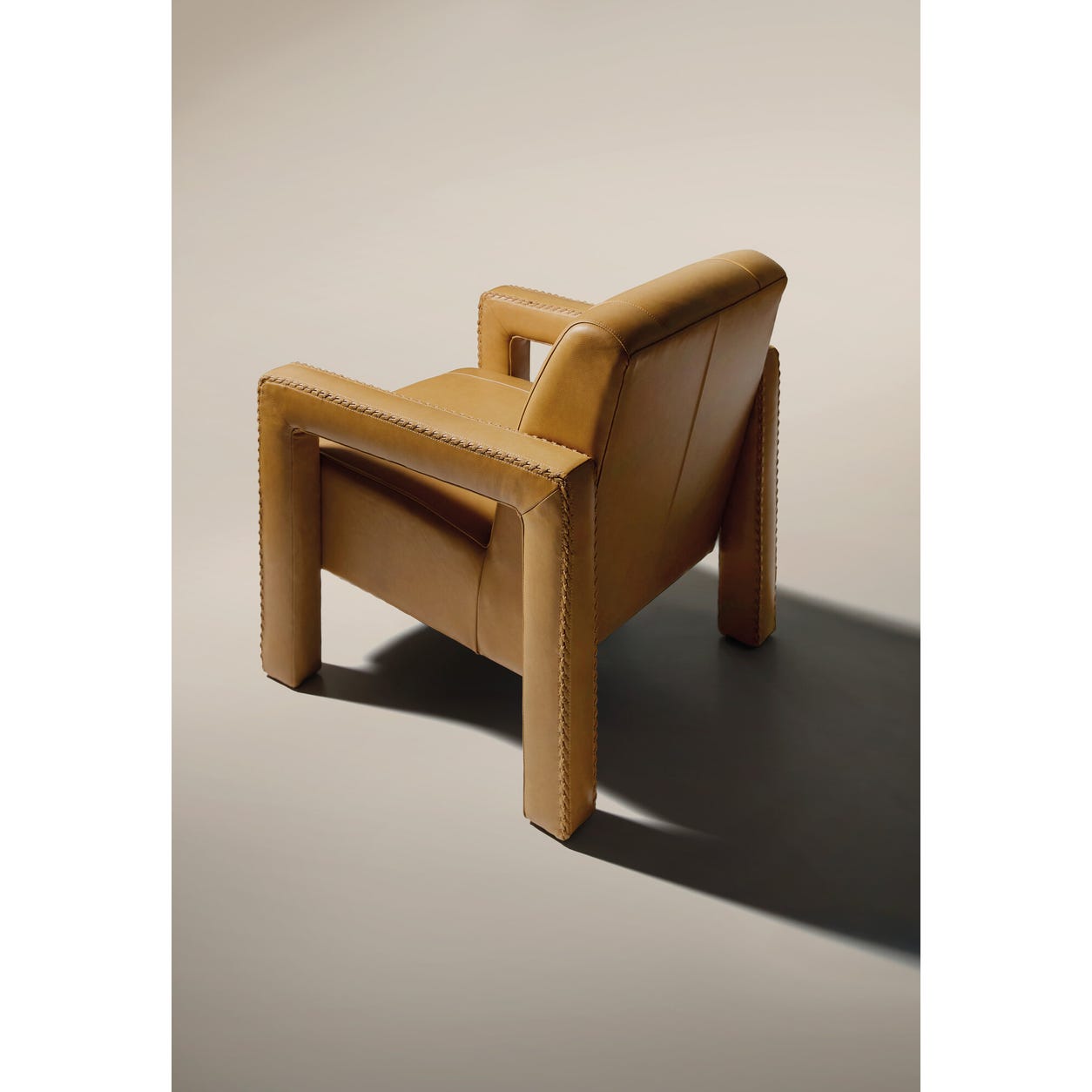 overhead view of a tan leather upholstered armchair with sturdy arms and detailed stitching on a white floor