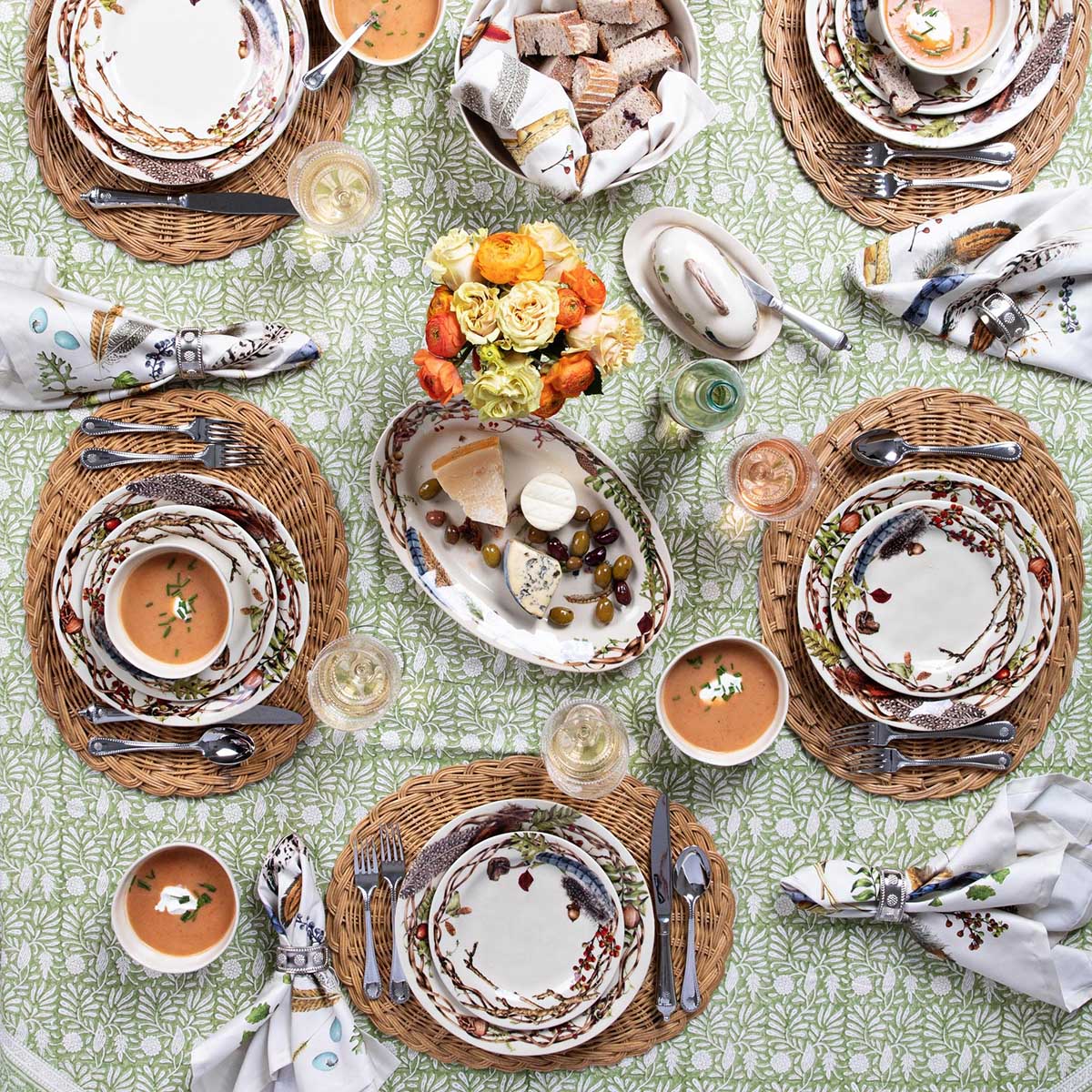 table set with woodland inspired plates and serving pieces on a green block print tablecloth