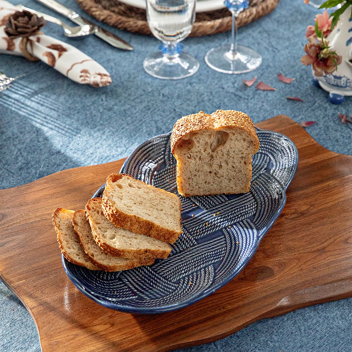 deep blue small hostess tray with intricate, interwoven braiding shown on a teak cutting board with bread