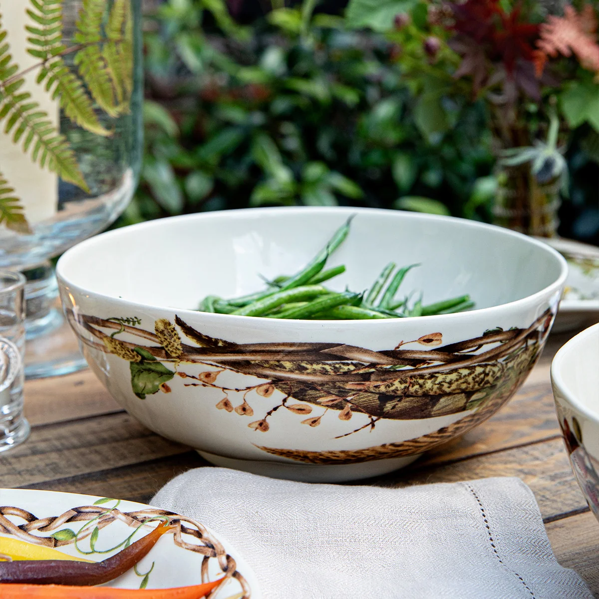 serving bowl with a painterly motif of flora, fauna, and found woodland treasures shown with green beans