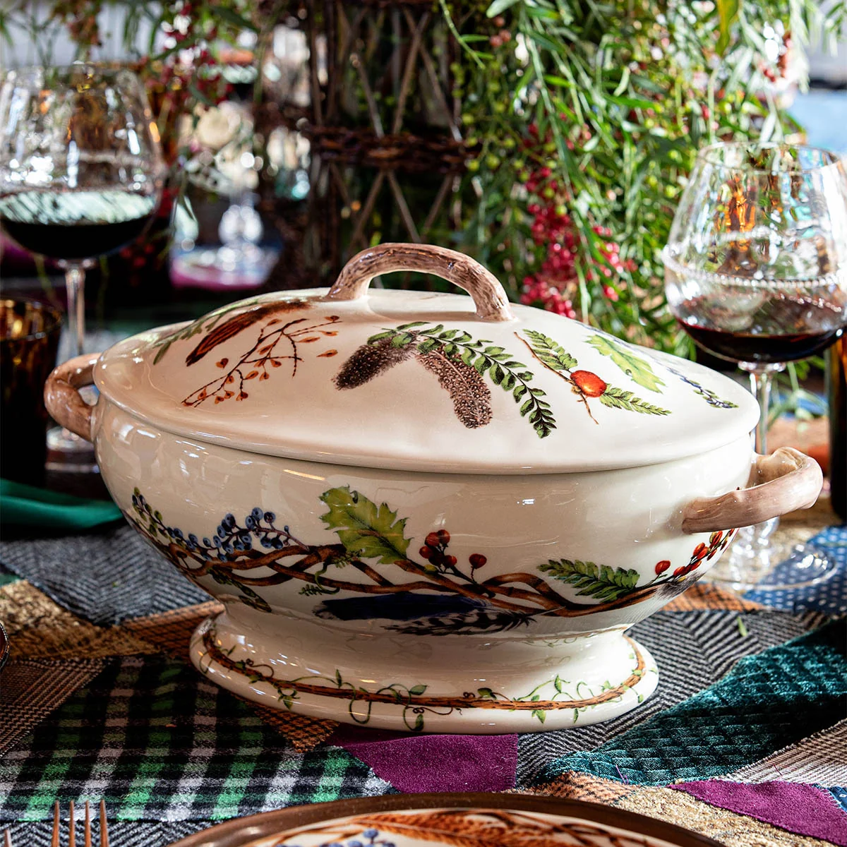 lidded tureen with faux-wooden handles and a painterly forest floor motif shown on a table with wine glasses