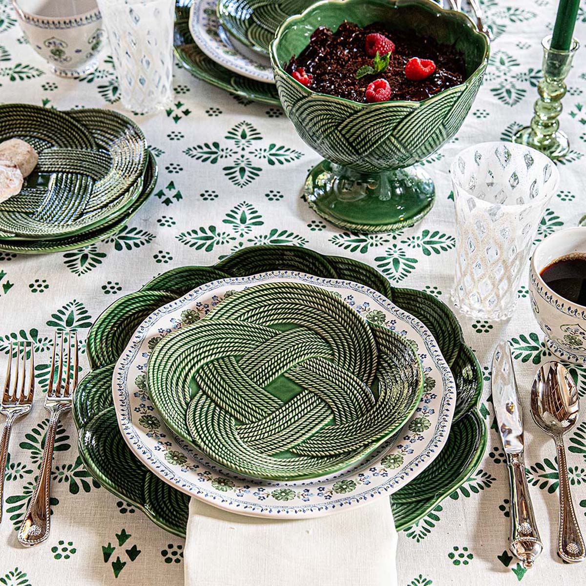 place setting with green interwoven braided whorls shown on a block printed green tablecloth