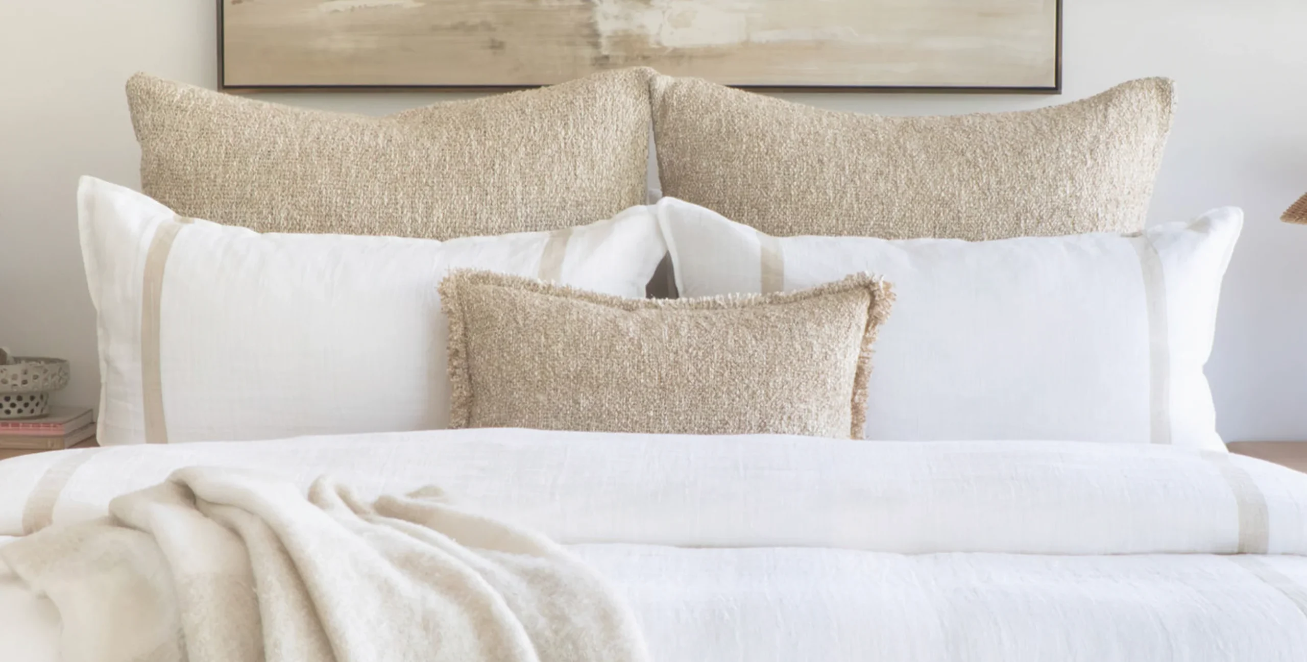bed made up with white linens and neutral textured chunky boucle decorative pillows