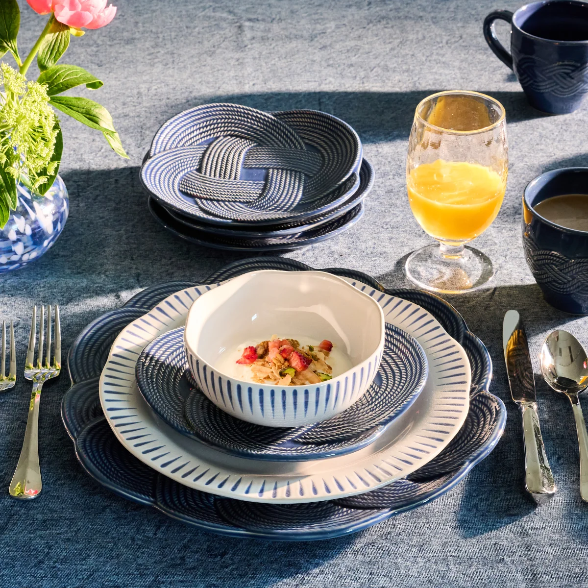 place setting with deep blue interwoven braided plates, plate and bowl with blue striped edges, and a glass of orange juice