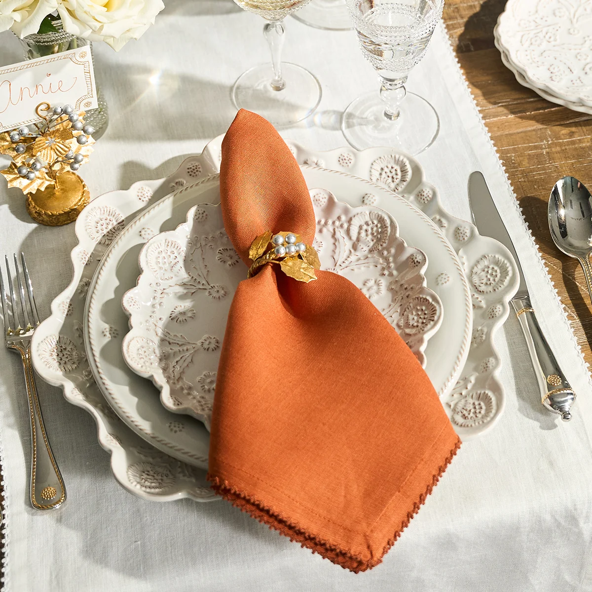 table set with ornate scalloped plates, silver and gold silverware, and an organe linen napkin