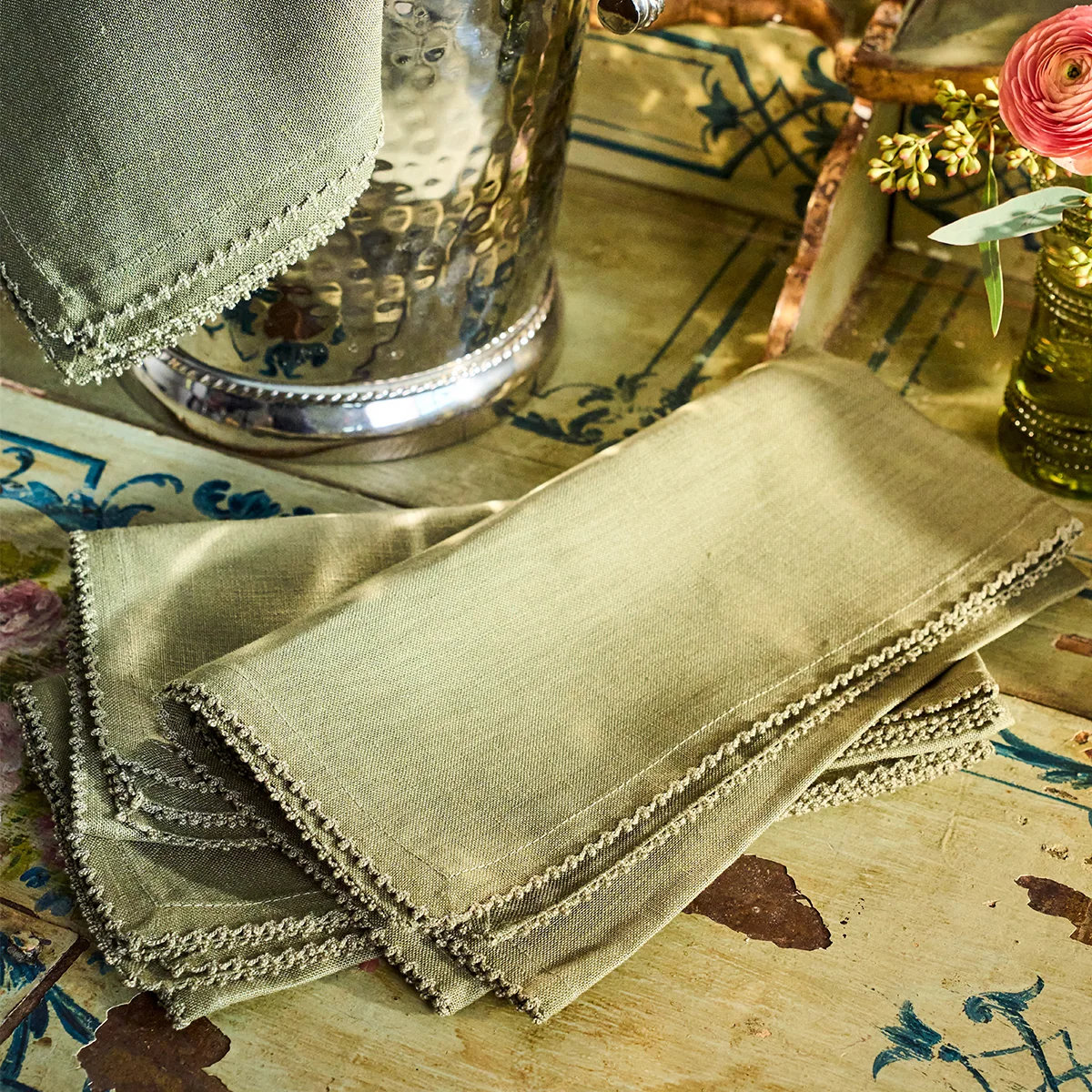 stack of sage green linen napkins with subtle scalloped edges on top of a painted surface