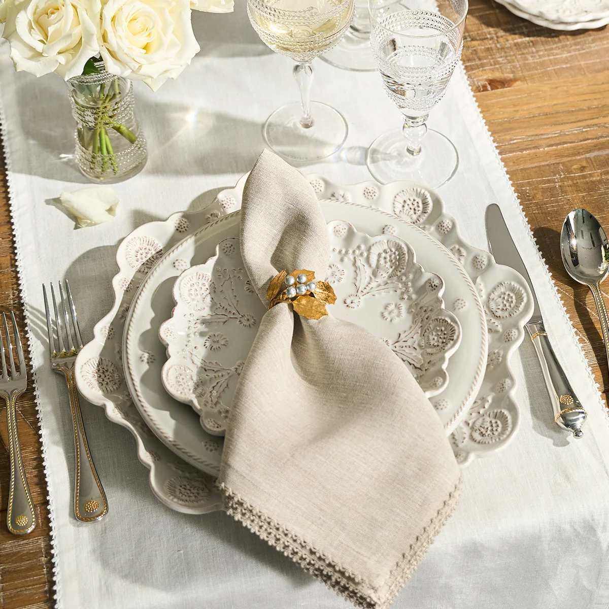 table set with ornate scalloped plates, silver and gold silverware, and a natural linen napkin