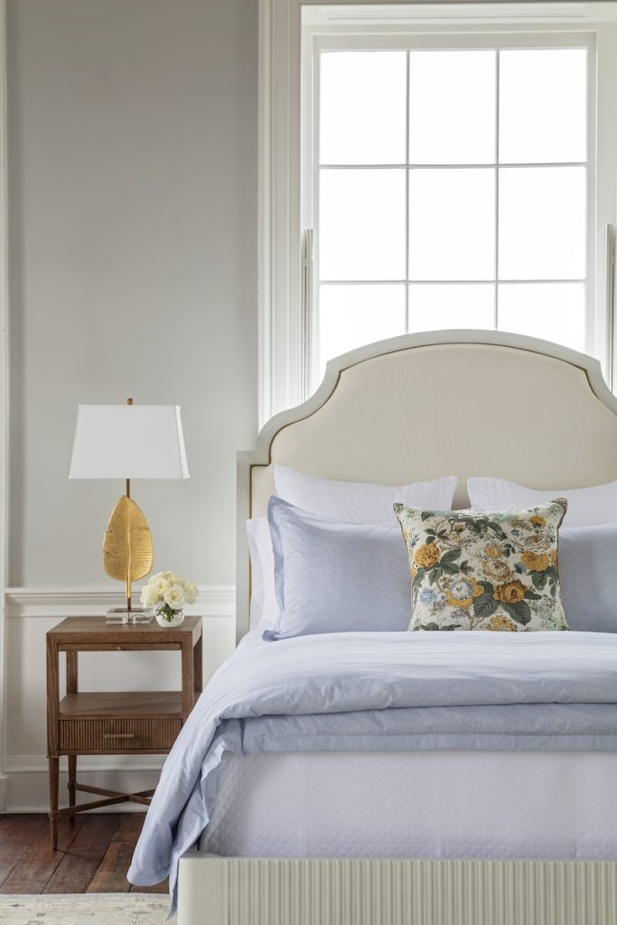 A bedroom styled in the quiet luxury interior design trend, furnished with a luxurious bed, an understated elegant bedside table, and subtly sculptural feather lamp.