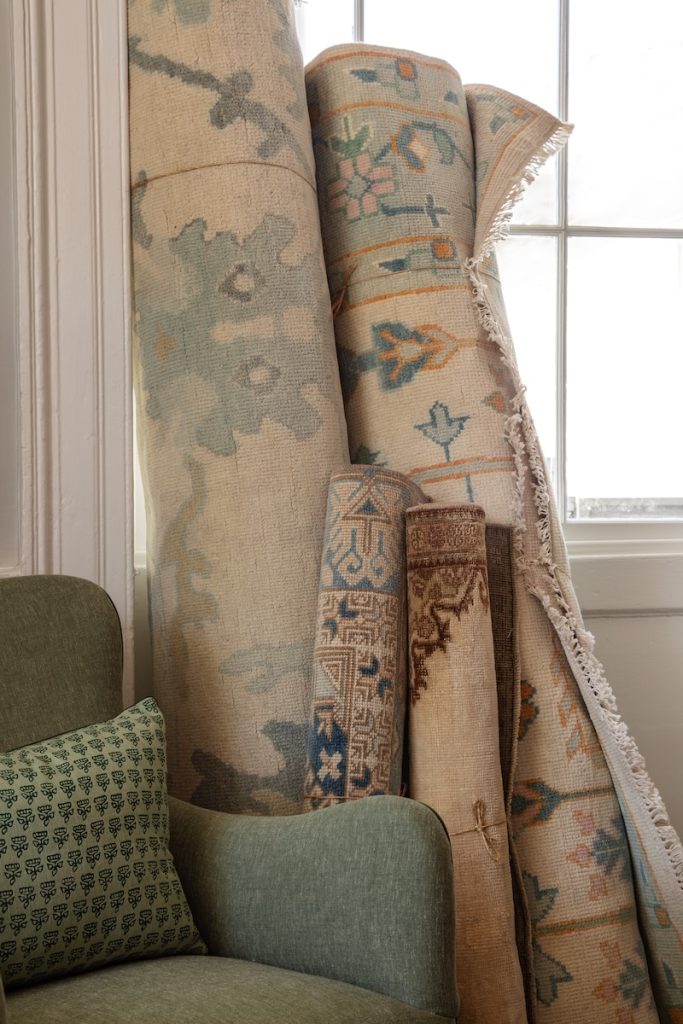a selection of rugs for sale in Charleston leans against a green armchair, with rich, luxurious textures and sophisticated patterns