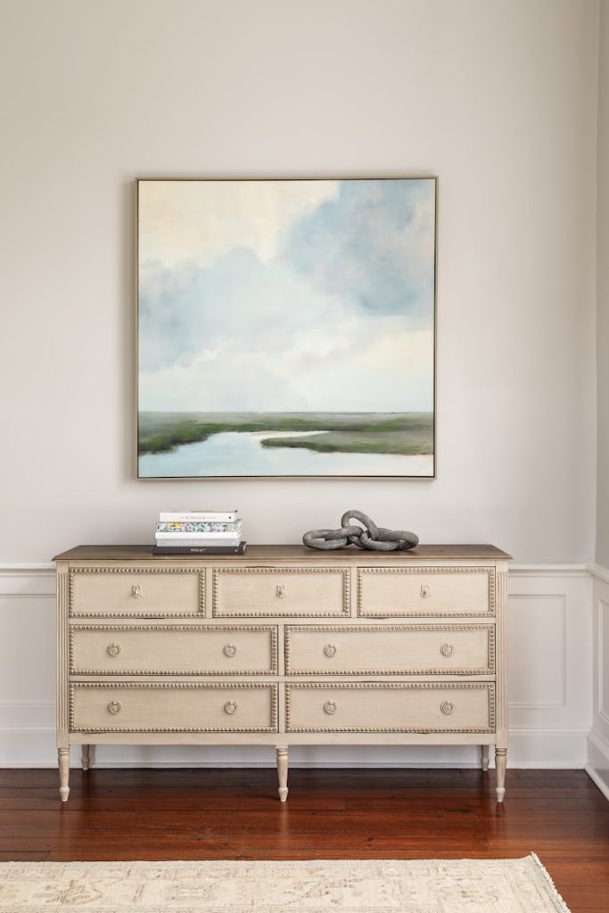 A chest of drawers in the antique-style quiet luxury design trend, styled with a Charleston marsh painting and home decor items