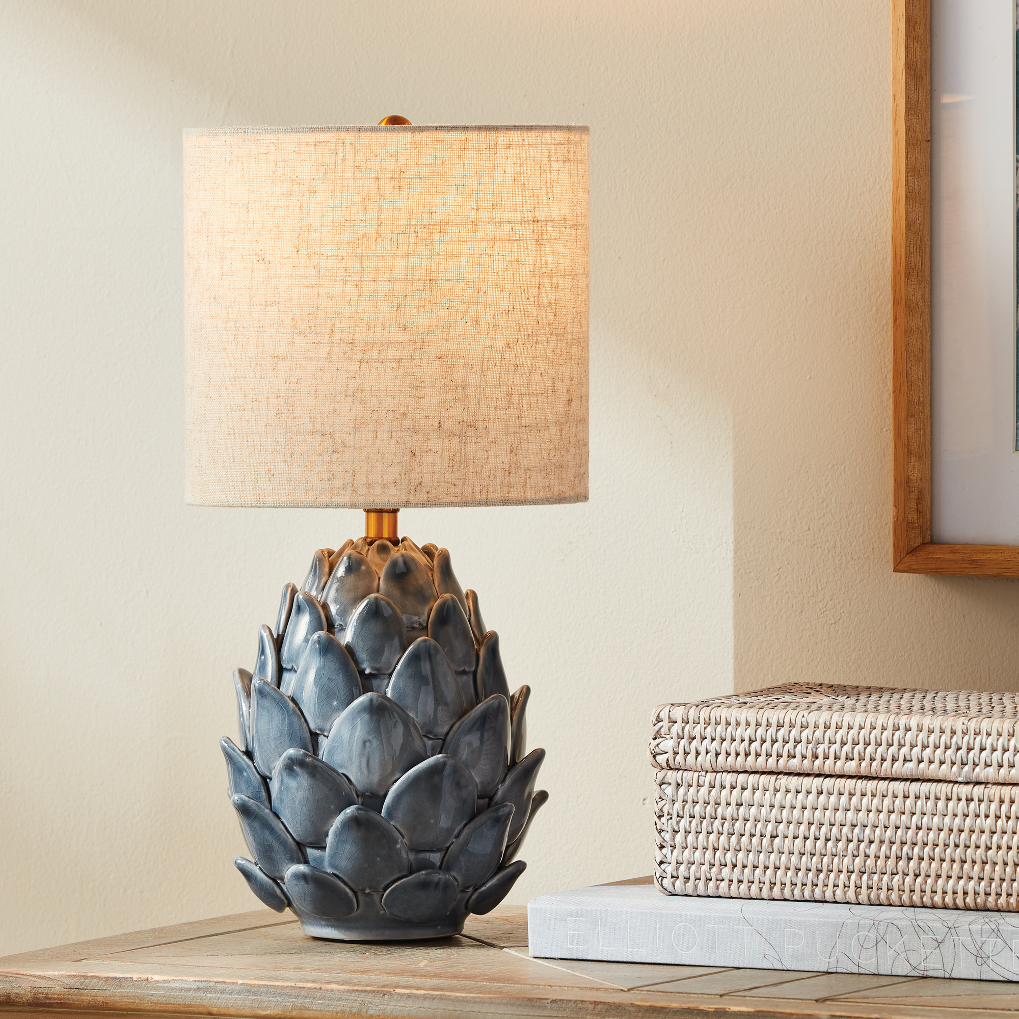 blue artichoke inspired lamp on a table with a book and woven box