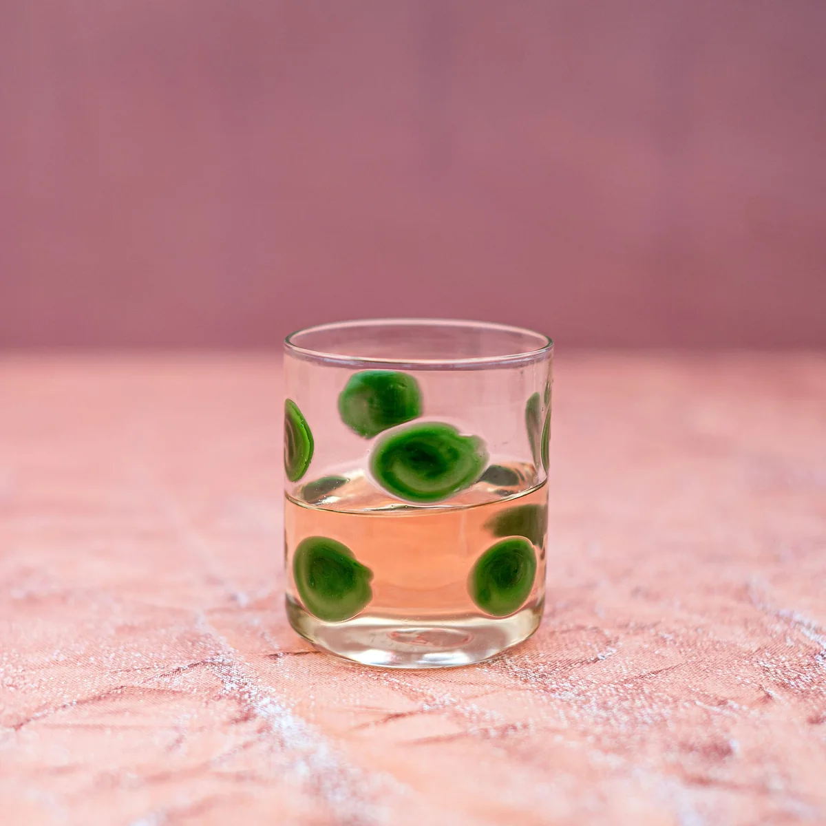 double old fashioned glass with green dots shown filled with a beverage in a neutral setting