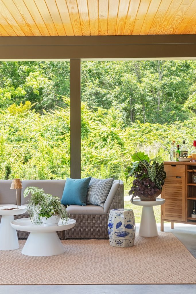 a covered patio with an outdoor rug, outdoor deep-seated sofa, modern outdoor tables, and patio bar cart, styled by the best furniture store Charleston has to offer: GDC