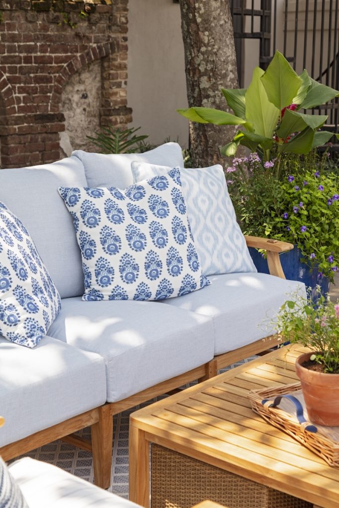 A deep-seated outdoor sofa styled with coastal home decor accessories in a tucked-away backyard lounge area, one of our favorite small outdoor space ideas for Charleston homes.