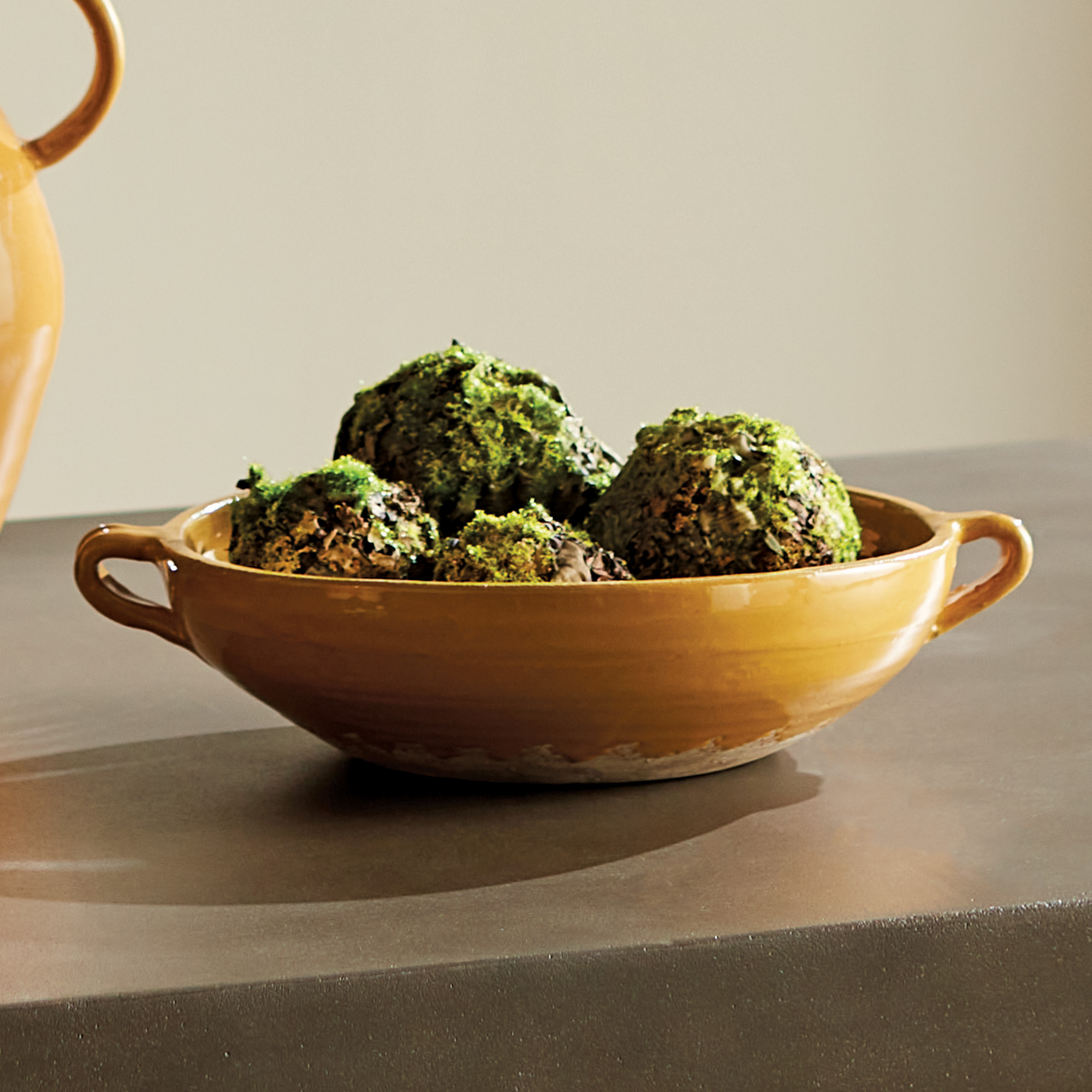 lifestyle image of decorative terracotta bowl with handles and golden ochre glaze, mossy orbs