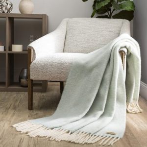 a soft woolen throw with white trim tossed over the arm of a chair