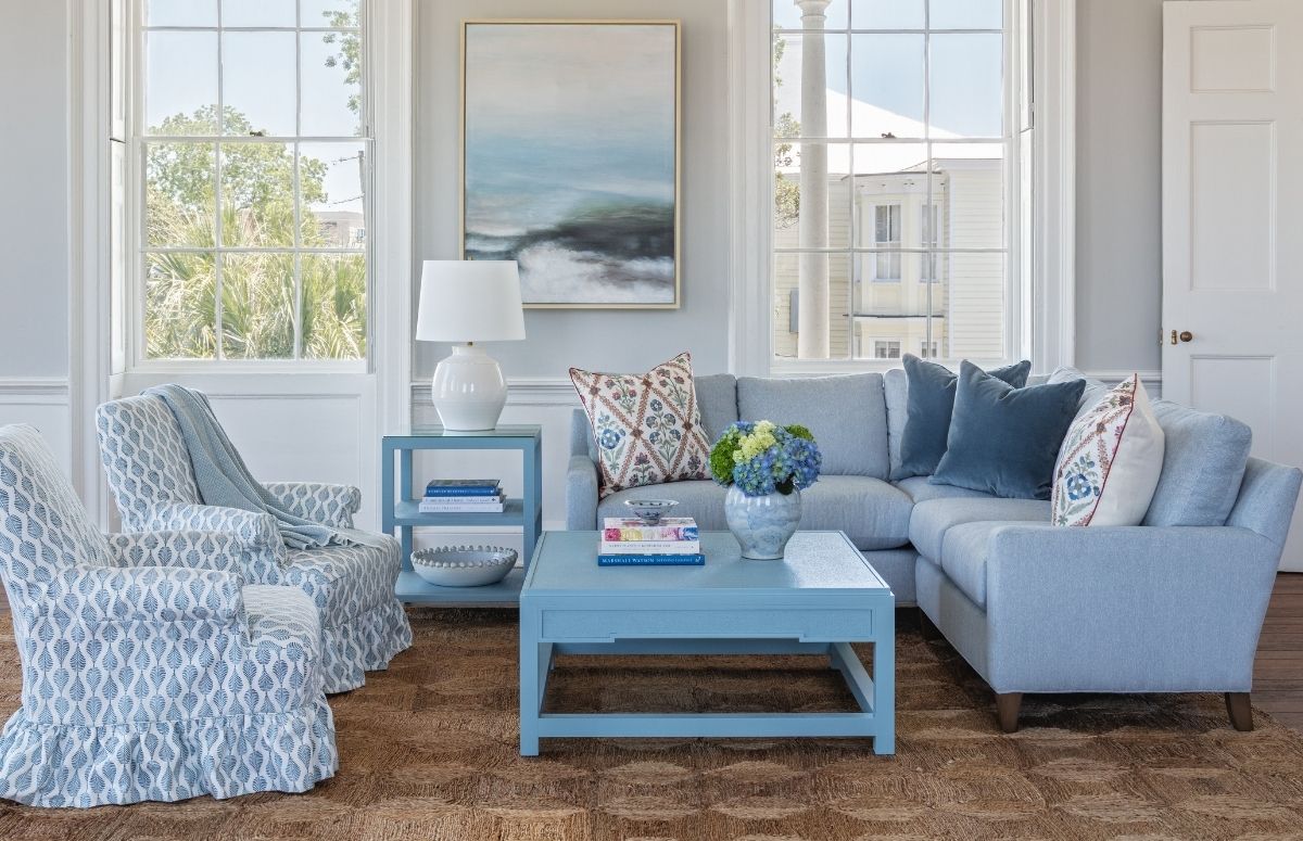 a coastal living room with blue and white armchairs, a blue side table, a blue coffee table, a light blue sectional with throw pillows, and decorative table lamps and coffee table books, styled by the best furniture store in Charleston