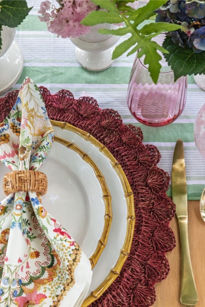 tabletop layout featuring deep red placemats, white dishes with bamboo trim, gold silverware and flatware, floral napkins, and coastal design table linens styled by the best furniture and gift store in Charleston