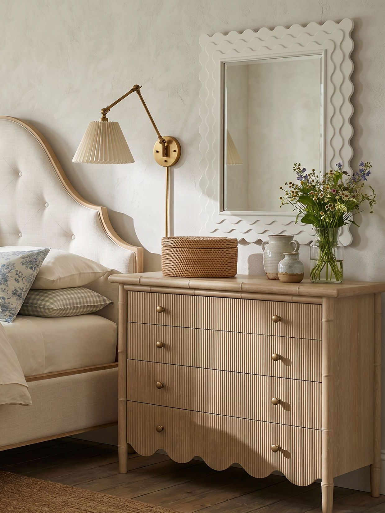bedroom with a scalloped bottom light wood chest, neutral upholstered bed, and pleated shade sconce