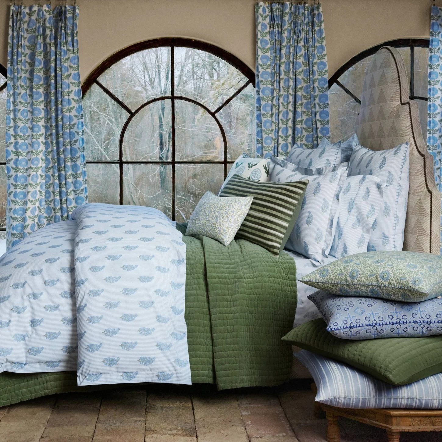 lifestyle image of light blue striped bedding with floral sprig pattern, green velvet quilt, block print curtains, accent bed pillows