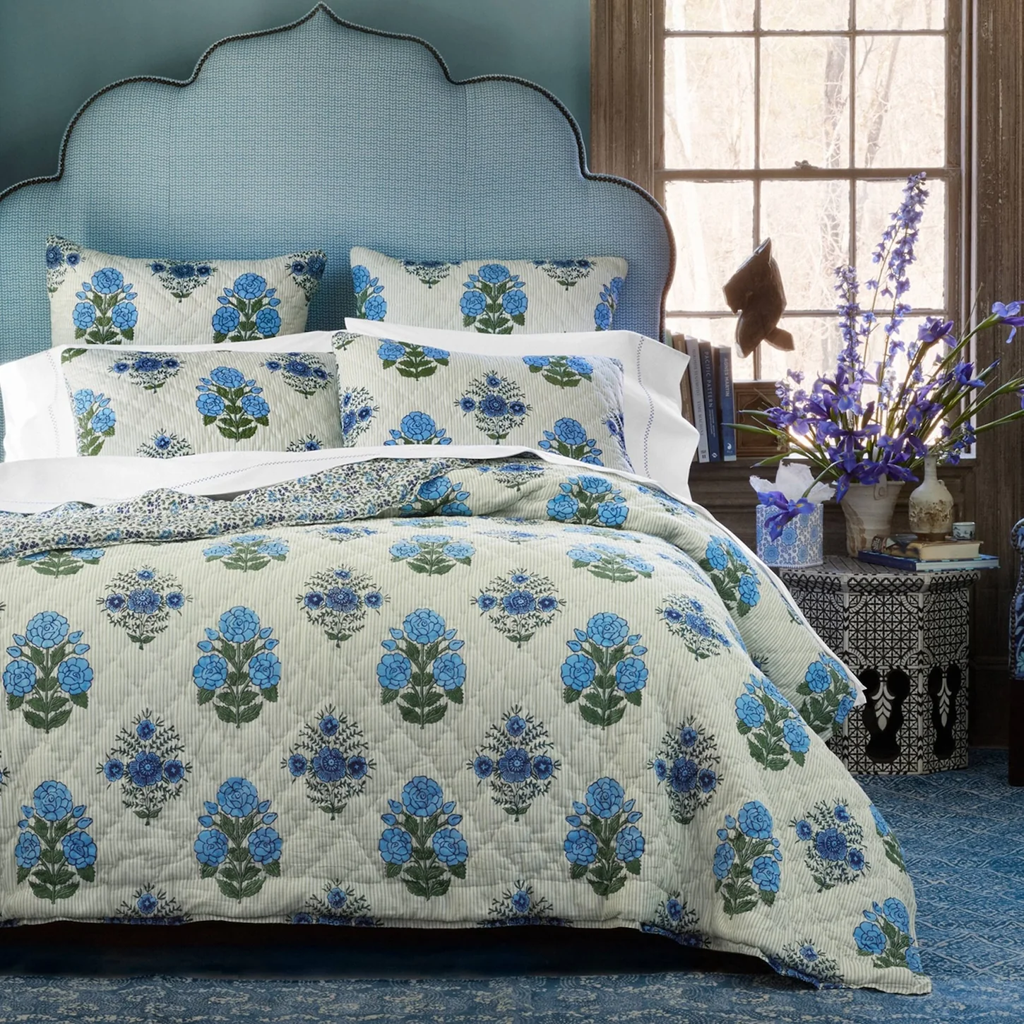 lifestyle image of light green striped quilt with blue block print flowers