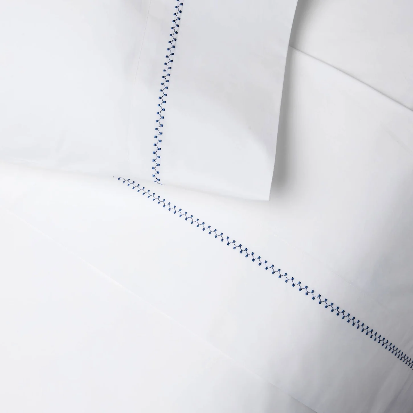 detail of white bedding with navy hand embroidery, sheets and pillowcases