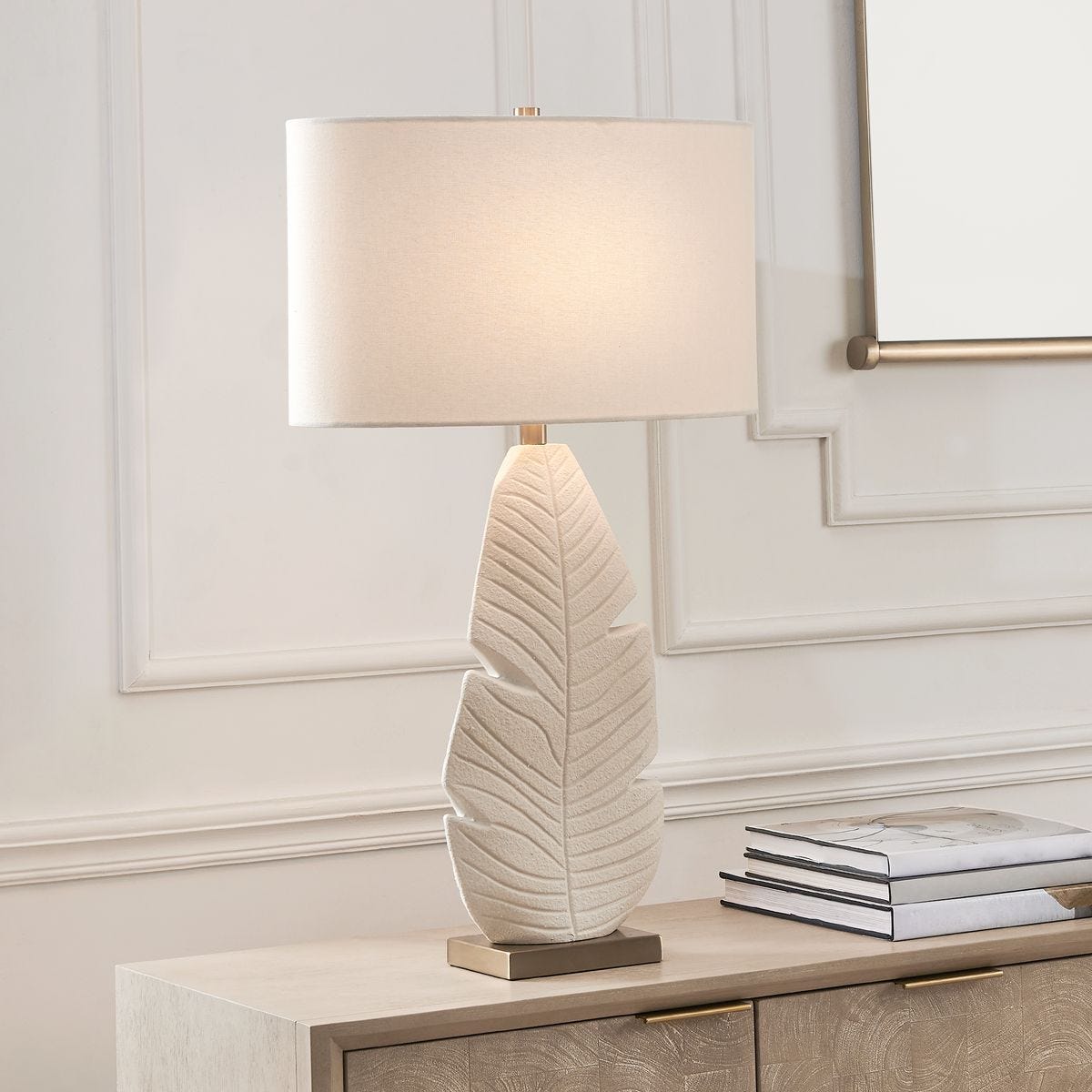 lifestyle image of table lamp with textured palm leaf motif and white shade