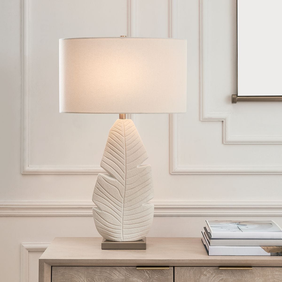 lifestyle image of table lamp with textured palm leaf motif and white shade