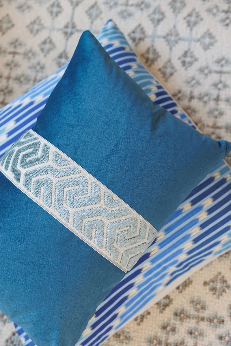 lifestyle image of navy velvet lumbar pillow with an aqua geometric embroidered center band