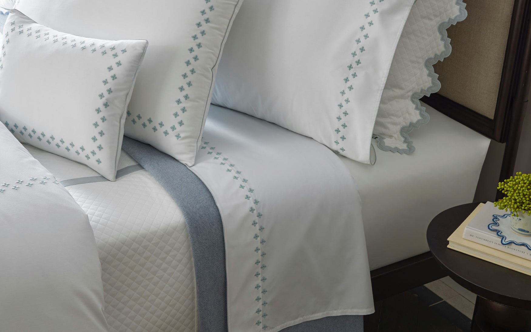 lifestyle image of bed with white bedding and pool embroidery on sheets and shams, Moroccan tilework, scalloped bedding