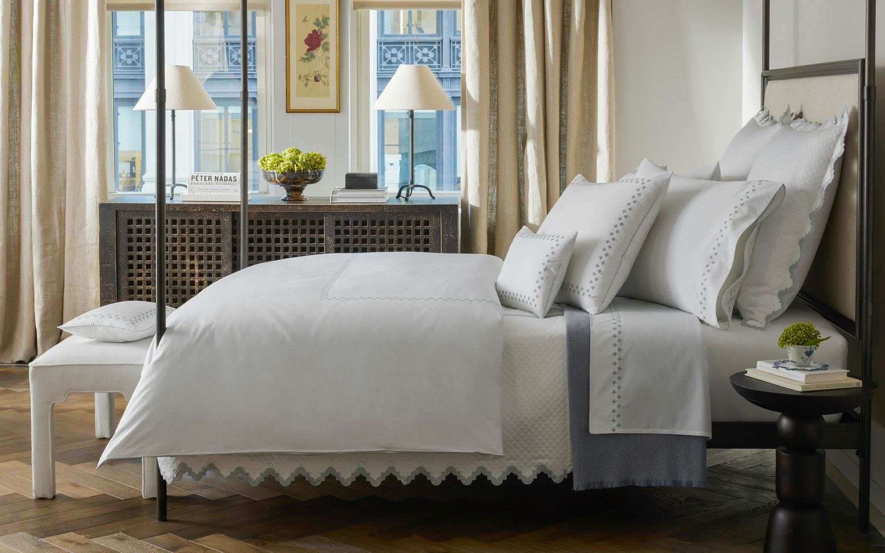 lifestyle image of bed with white bedding and pool embroidery on shams and duvet, Moroccan tilework, scalloped bedding