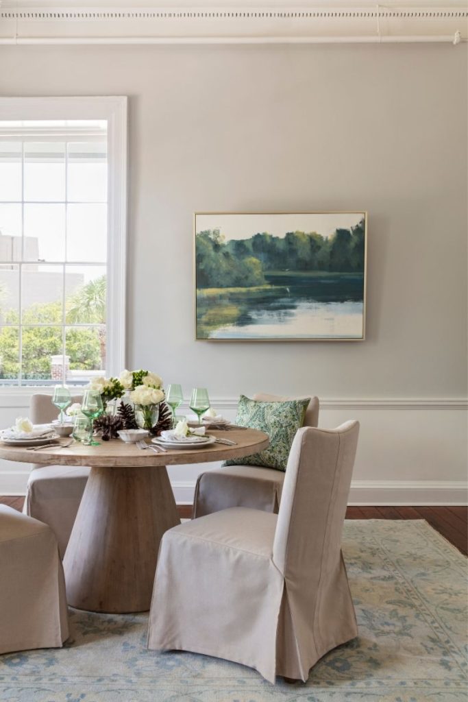 A dining room furniture setup styled with slipcover dining chairs, a round dining table, and light colored rugs in Charleston, SC