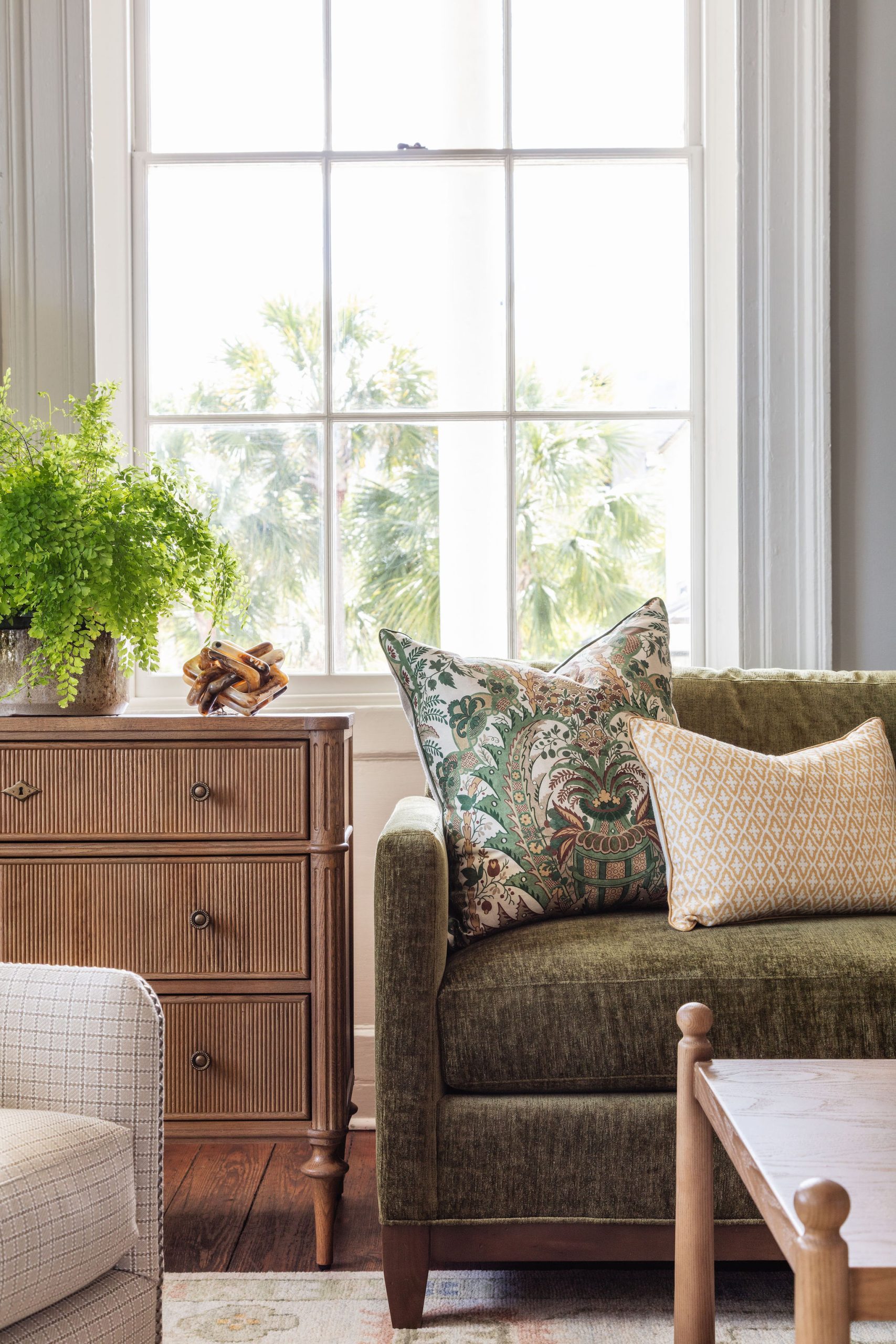 lifestyle image of oak chest with pencil ribbed drawer fronts, greenery, and yellow and green decorative pillows on a green velvet sofa