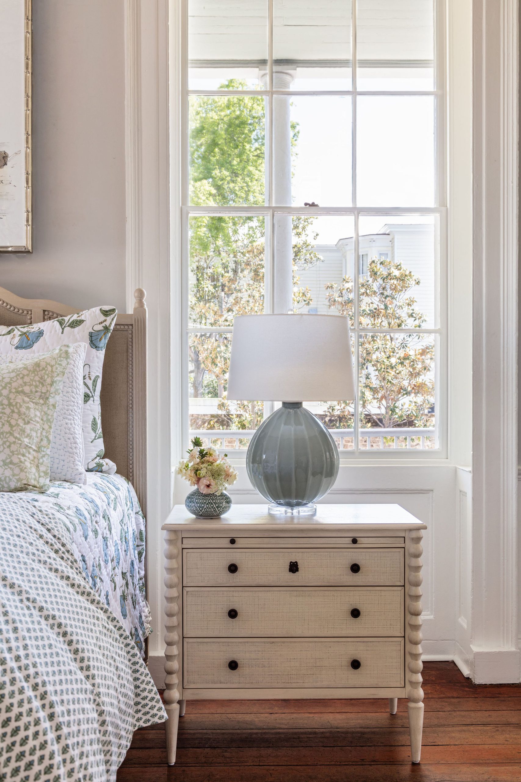 lifestyle image of nightstand with linen front drawers in a chalk white finish, teal lamp, and block print bedding