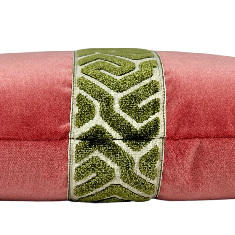 Side view of a bright coral velvet lumbar pillow with a green geometric embroidered center band