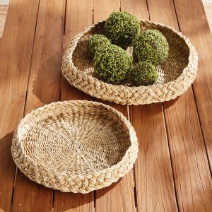 lifestyle picture of a pair of braided abaca round trays displayed with decorative moss balls