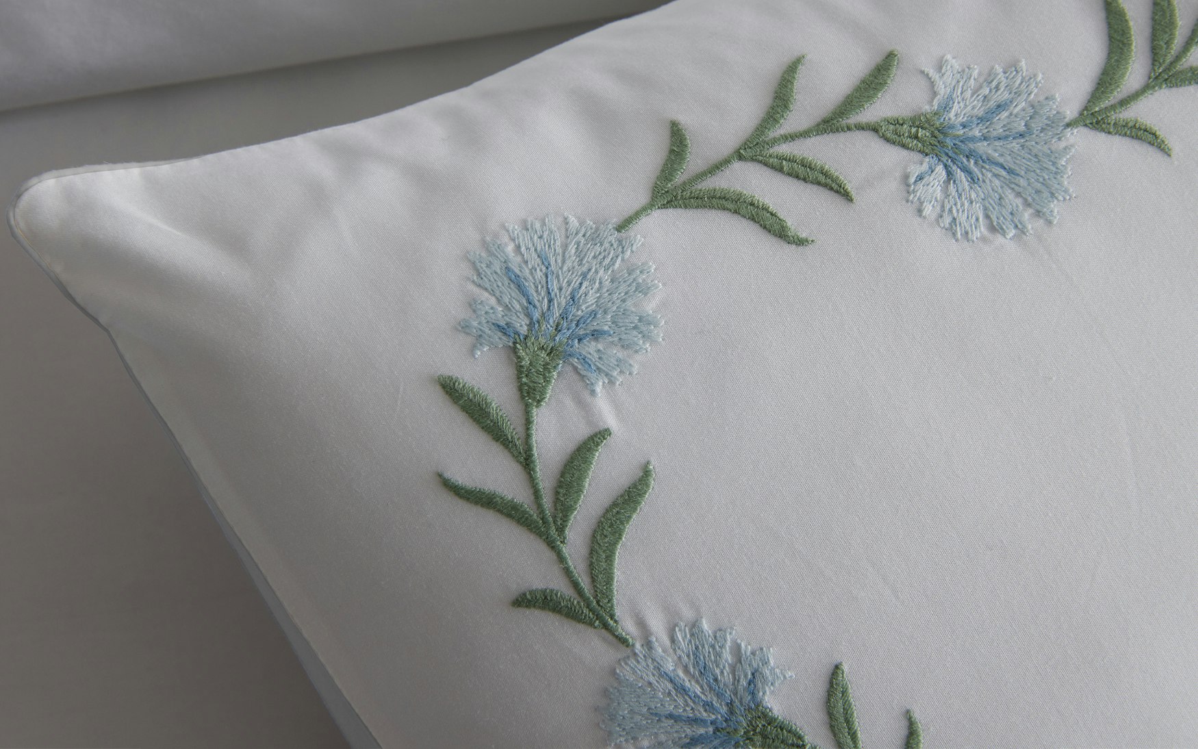 detail of light blue and green floral vine embroidery on a white pillow sham