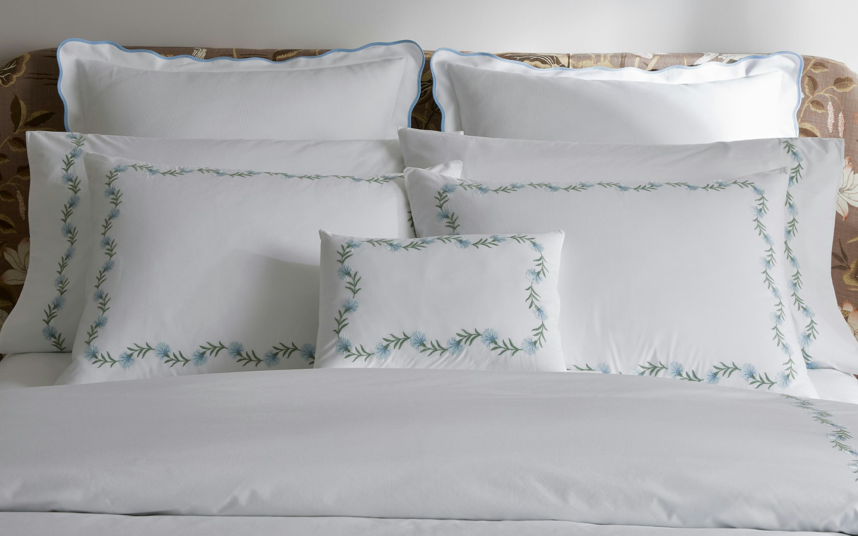 lifestyle image of a bed made up with light blue and green floral vine embroidery bedding