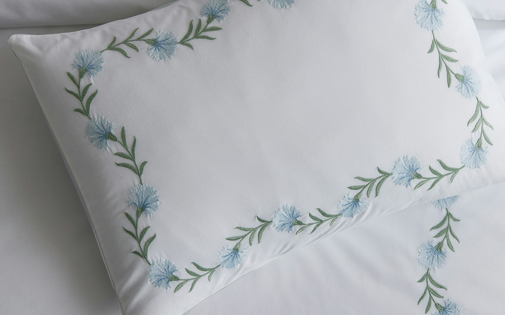 detail of light blue and green floral vine embroidery on a white pillow sham