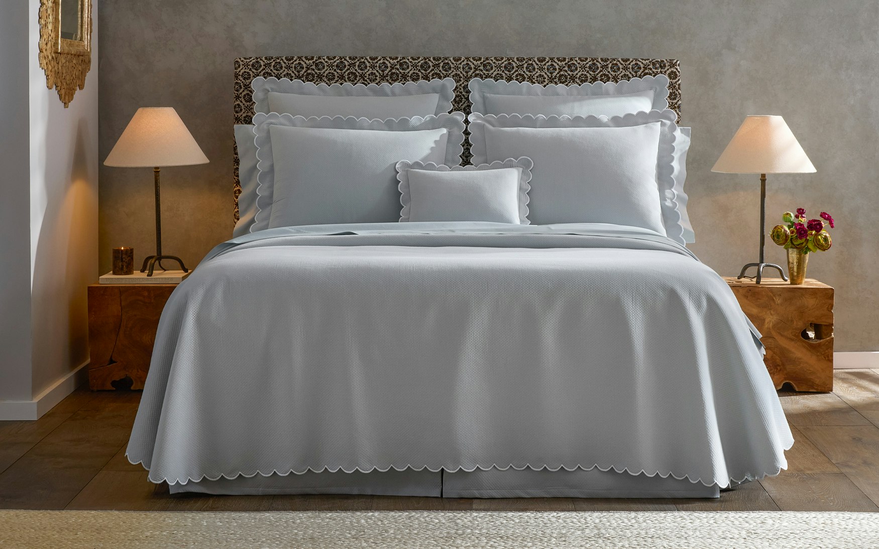 lifestyle image of a bed made up in light blue bedding with scalloped edges