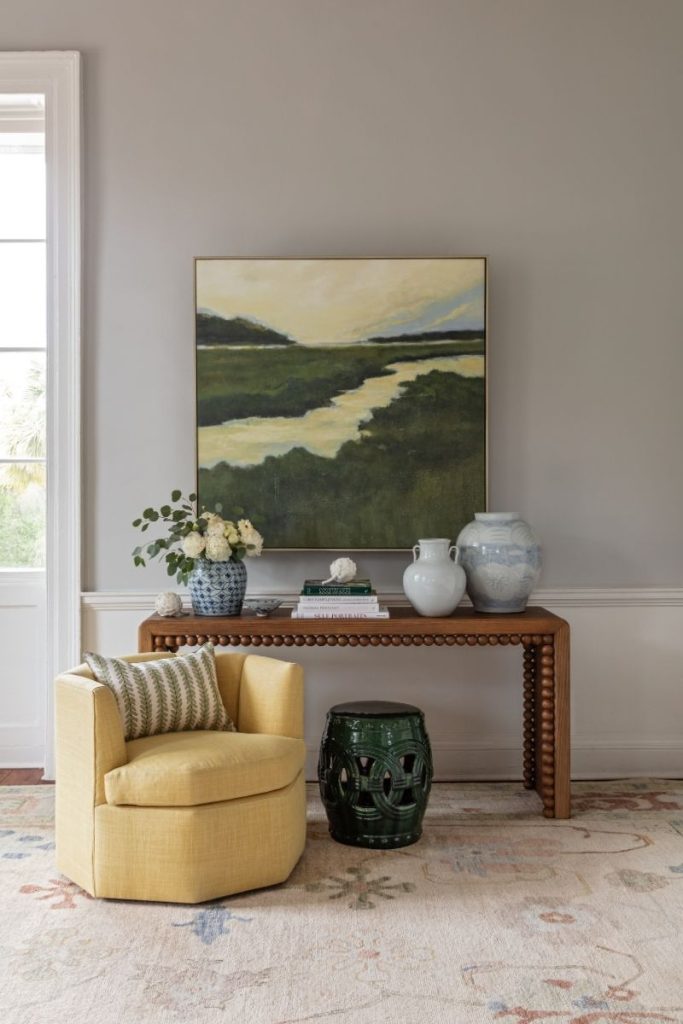 A Charleston furniture setup styled with a custom accent chair in yellow upholstery as a centerpiece, with a garden stool, marsh painting, and Charleston home decor