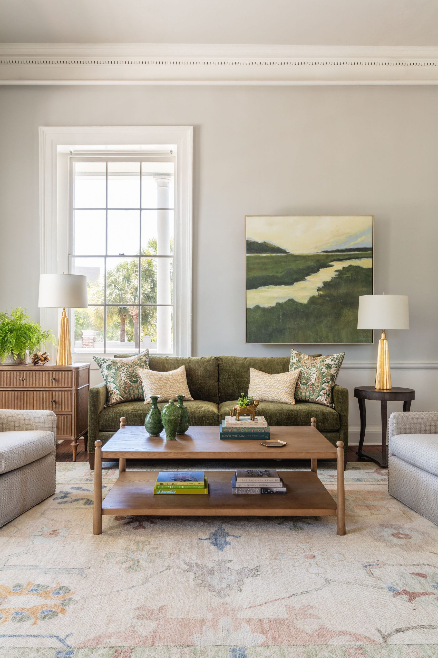 lifestyle image of a living room, green sofa, coffee table, marsh sunset painting, gold lamps, decorative pillows, pastel colored rug
