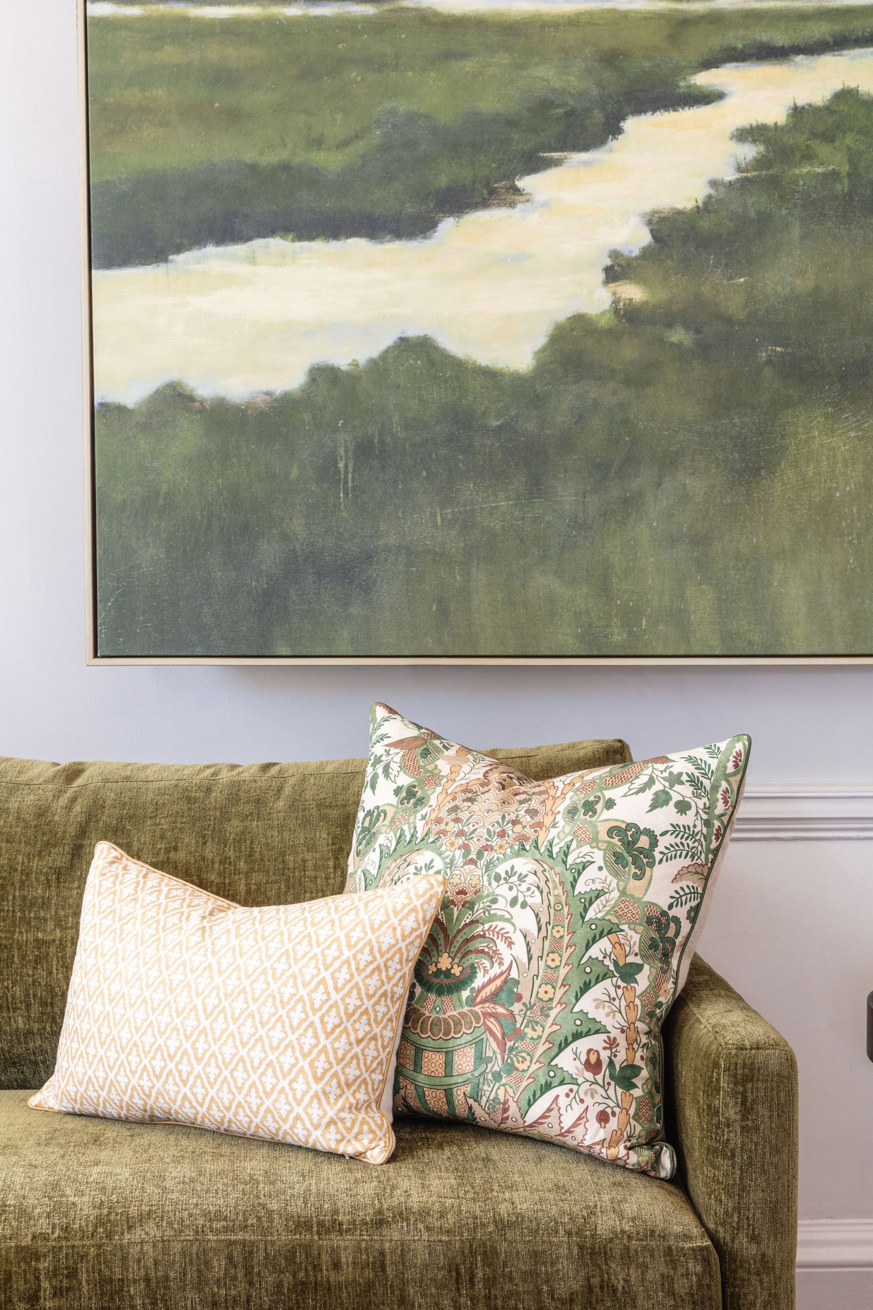 lifestyle image of a green sofa, yellow and green decorative pillows, and a marsh sunset painting